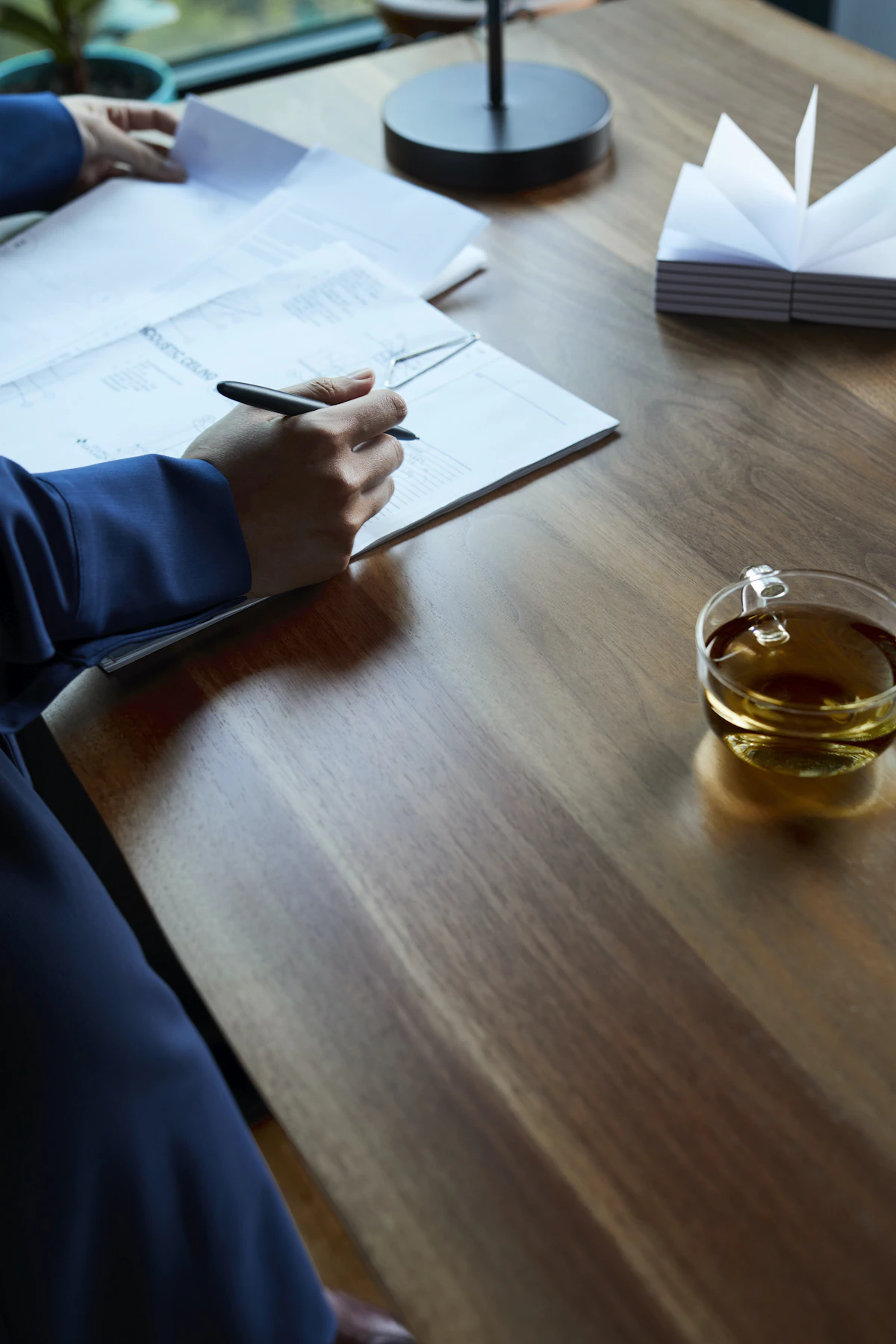 A person working through paperwork at a desk beside a laptop