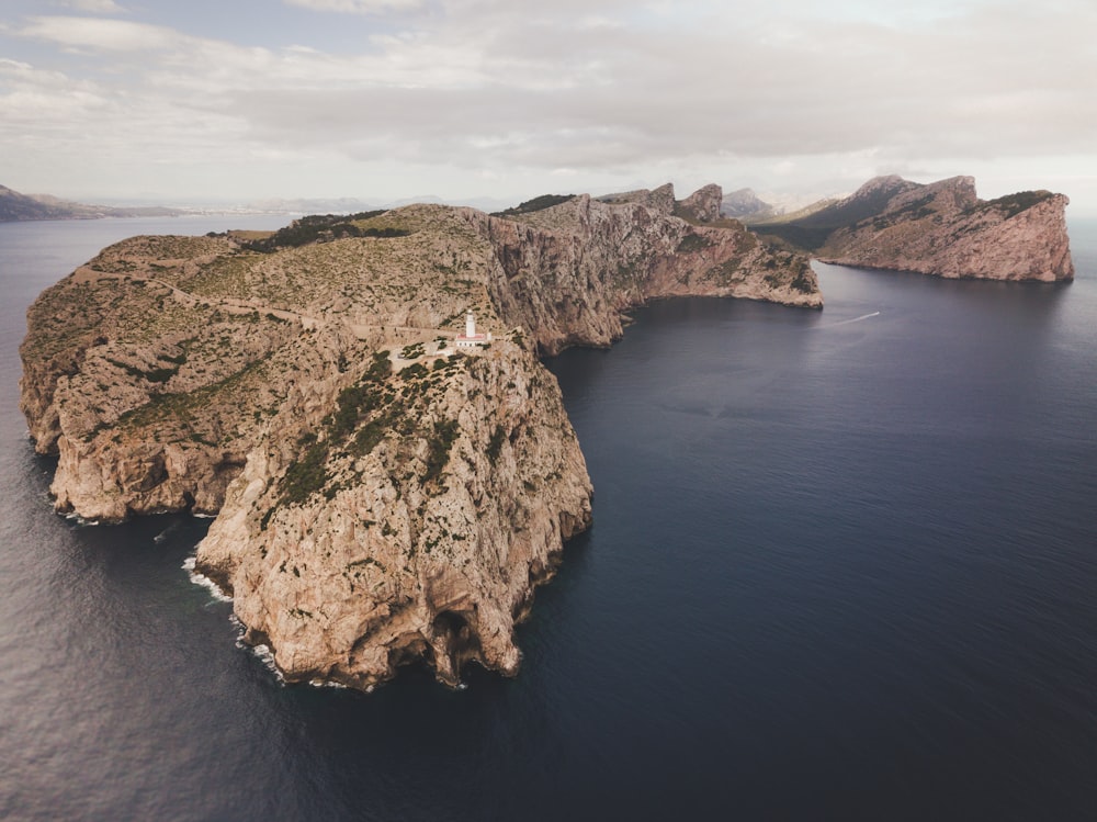 brown and green mountain beside blue sea under white clouds during daytime