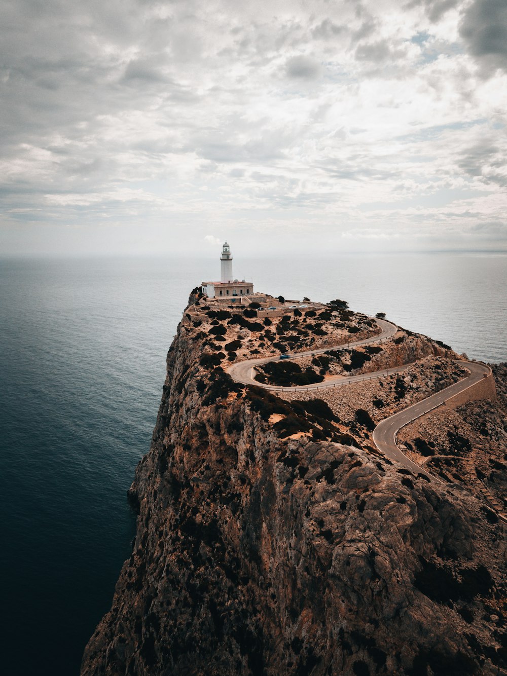 white and brown lighthouse on brown rock formation near body of water during daytime