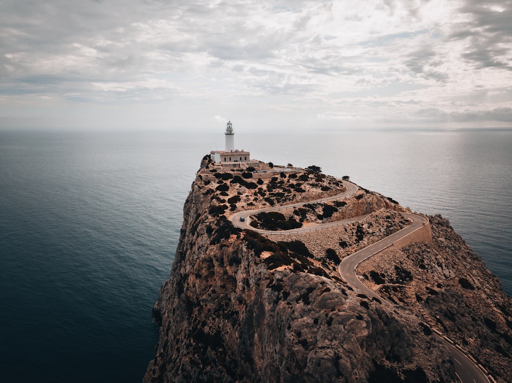 Faro blanco en la montaña rocosa marrón cerca del cuerpo de agua durante el día