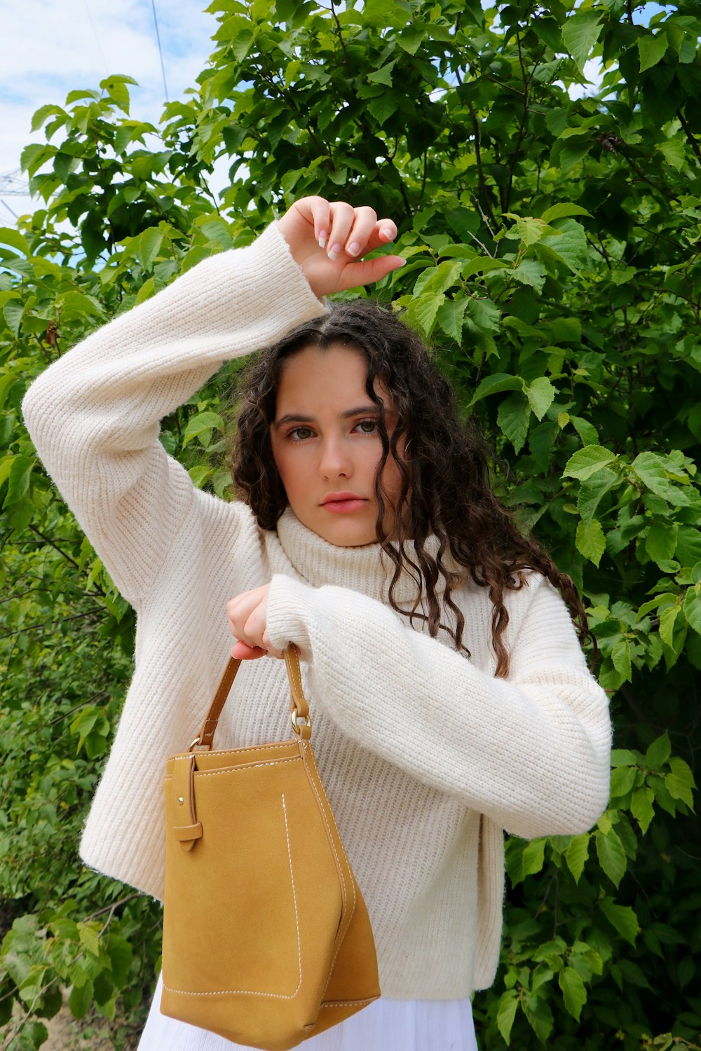 woman in white sweater holding brown leather sling bag