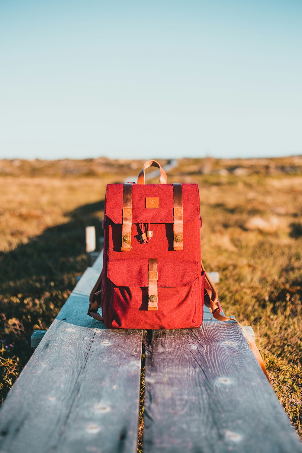 a red backpack sitting on top of a wooden bench