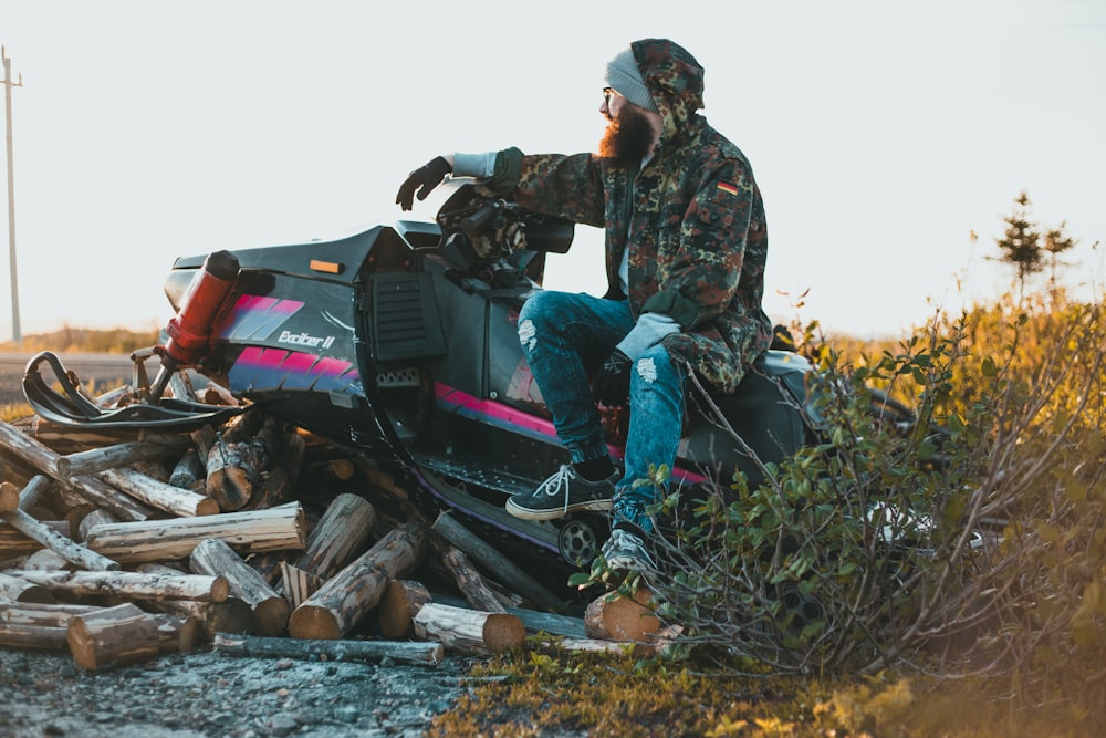 a man riding on the back of a motorcycle next to a pile of logs