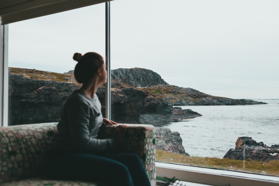 woman in gray jacket sitting on chair looking at the sea during daytime