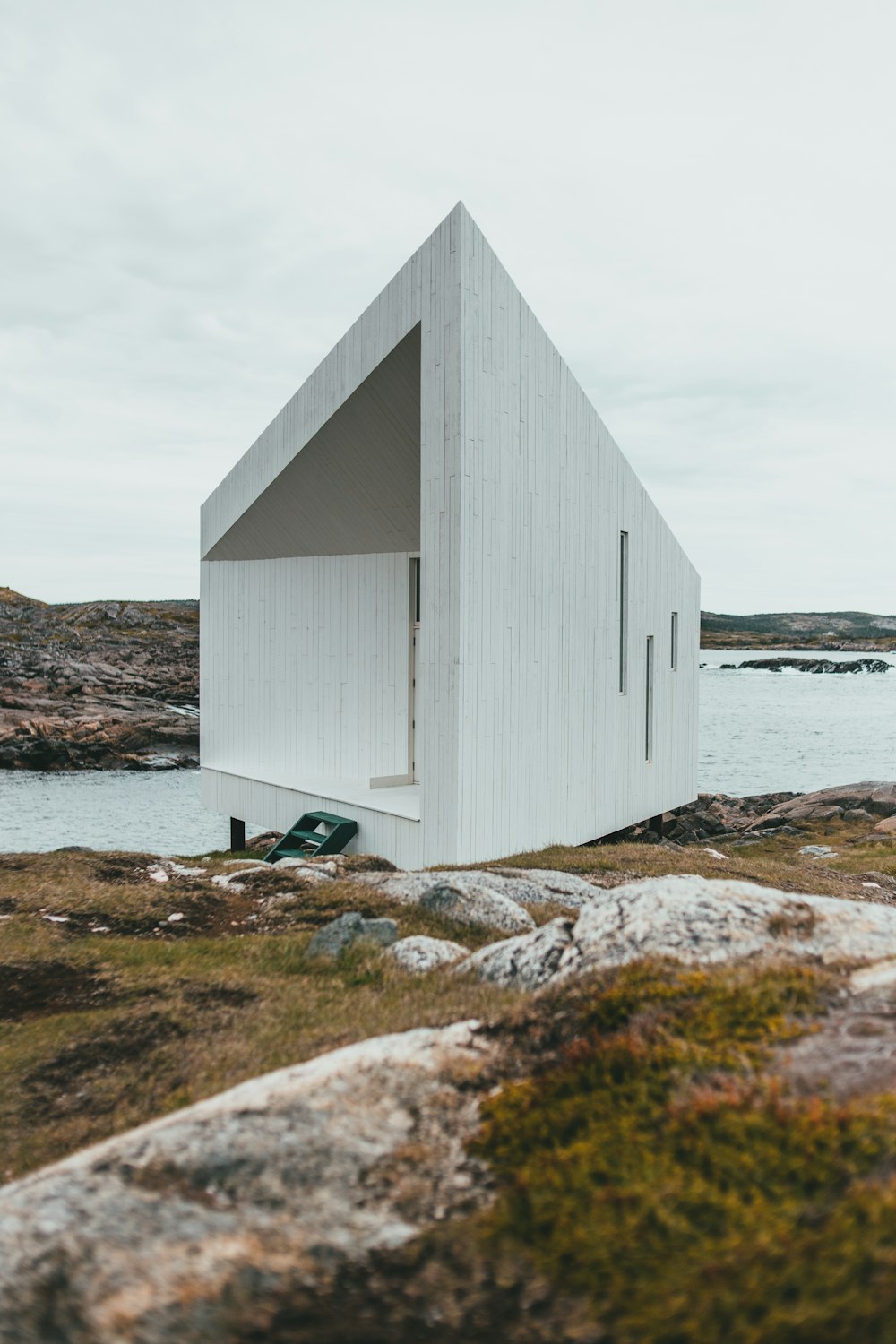 white wooden house on green grass field near body of water during daytime