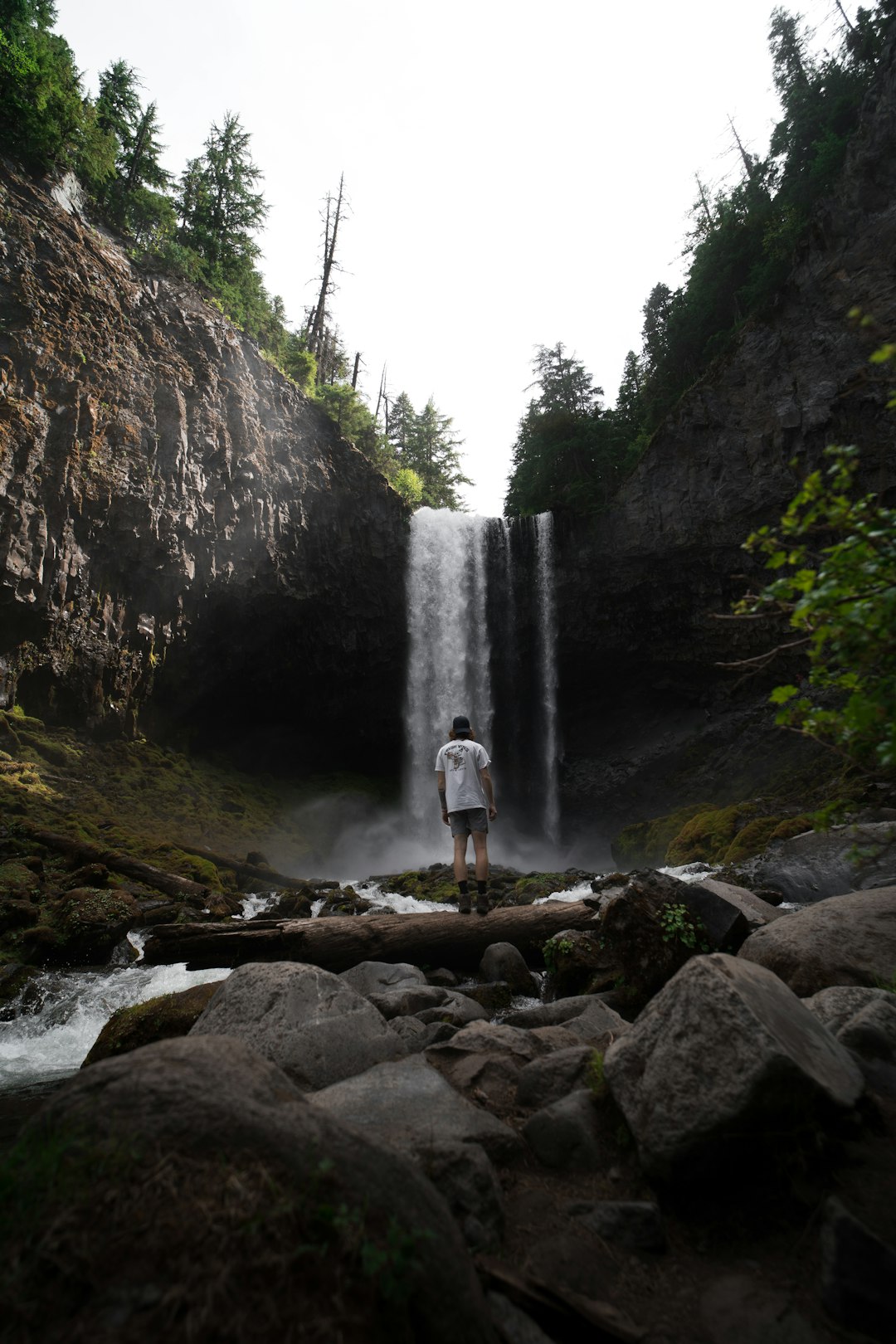 person in white shirt standing on brown rock near waterfalls during daytime