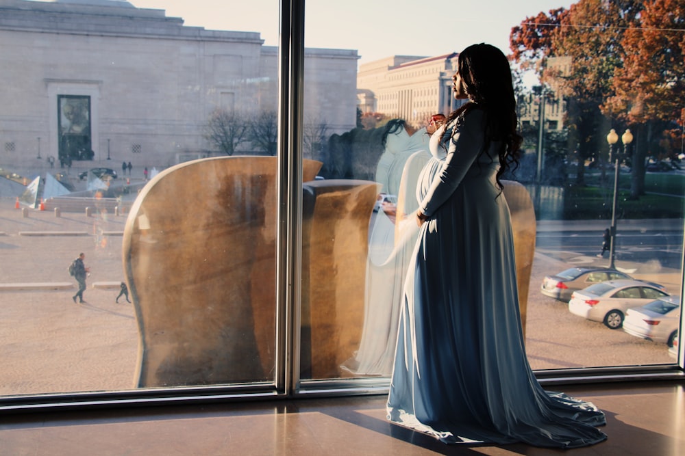 woman in black dress standing near glass window