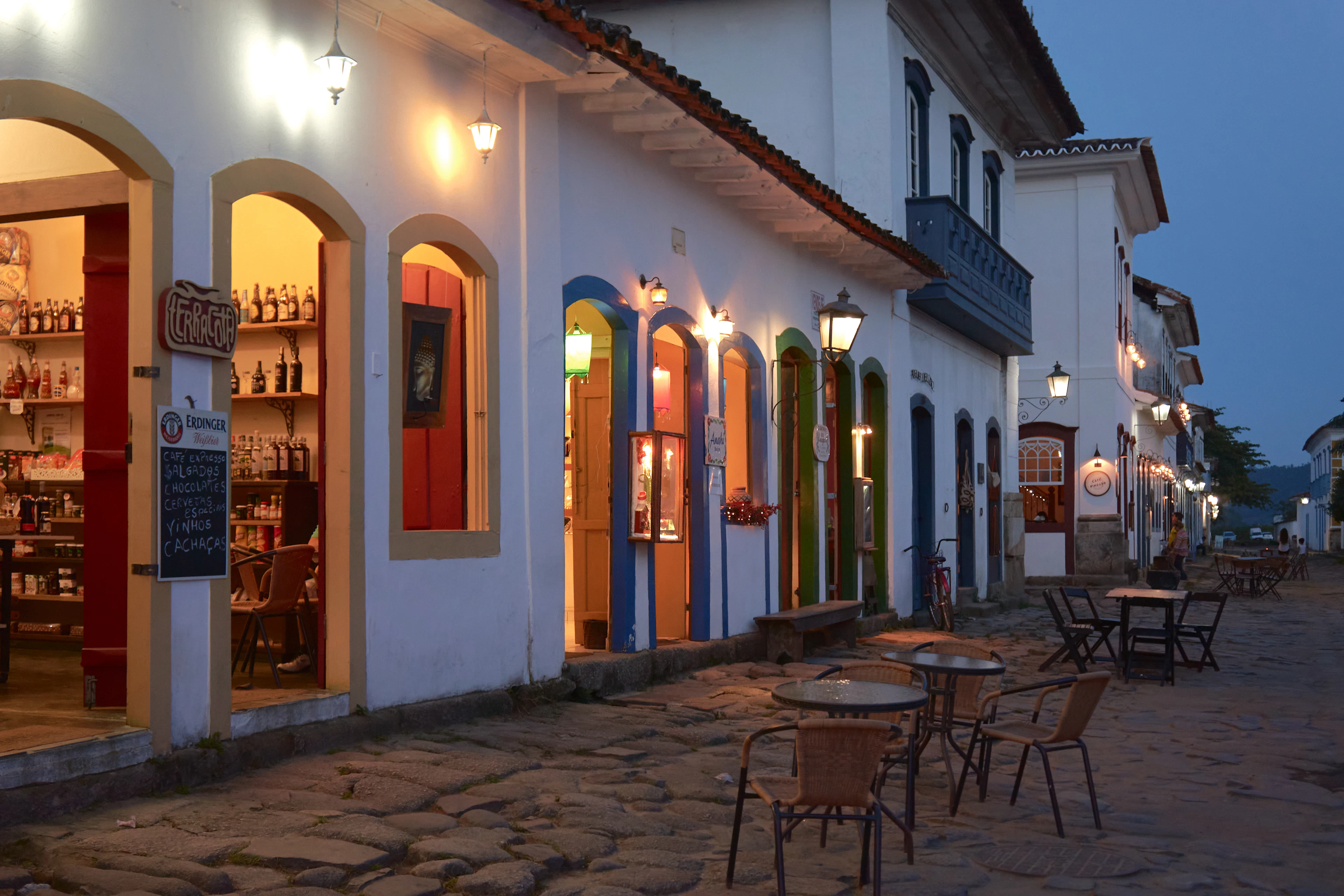 Akmenimis grįsta istorinio Paračio centro gatvė su staliukais ir apšviestomis durimis prieblandoje, Brazilija
