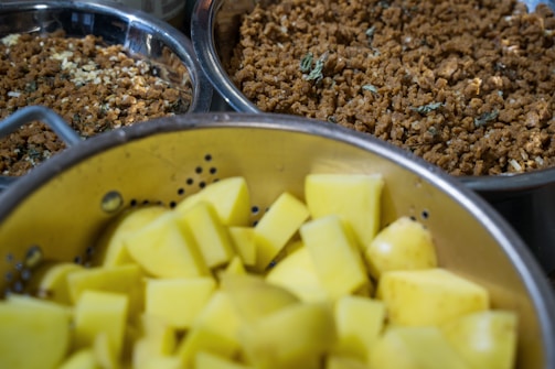 Three stainless steel bowls contain chopped potatoes and crumbled ground meat, possibly seasoned with herbs. The ingredients are likely being prepared for a recipe.