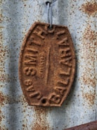 A weathered, rusted metal tag with embossed lettering, attached to a corrugated metal surface. The tag features the words 'JAS SMITH BALLARAT.' The metal surface also appears rusted, adding texture and character to the scene.