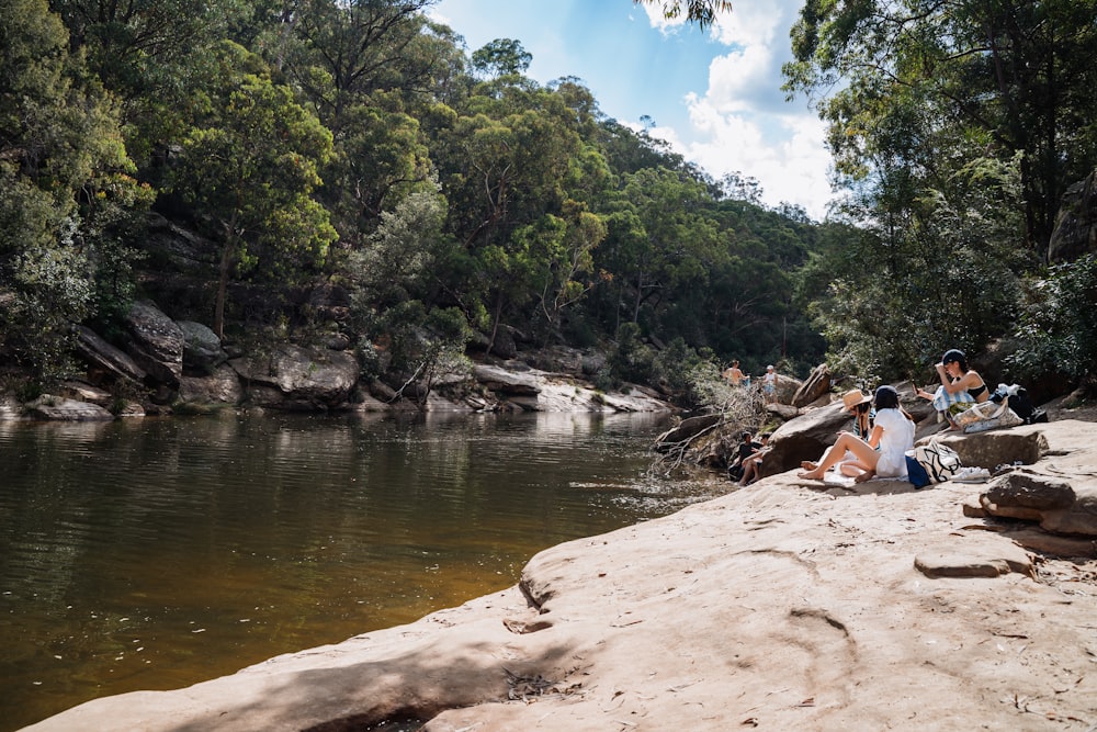 a group of people sitting on a rock next to a river