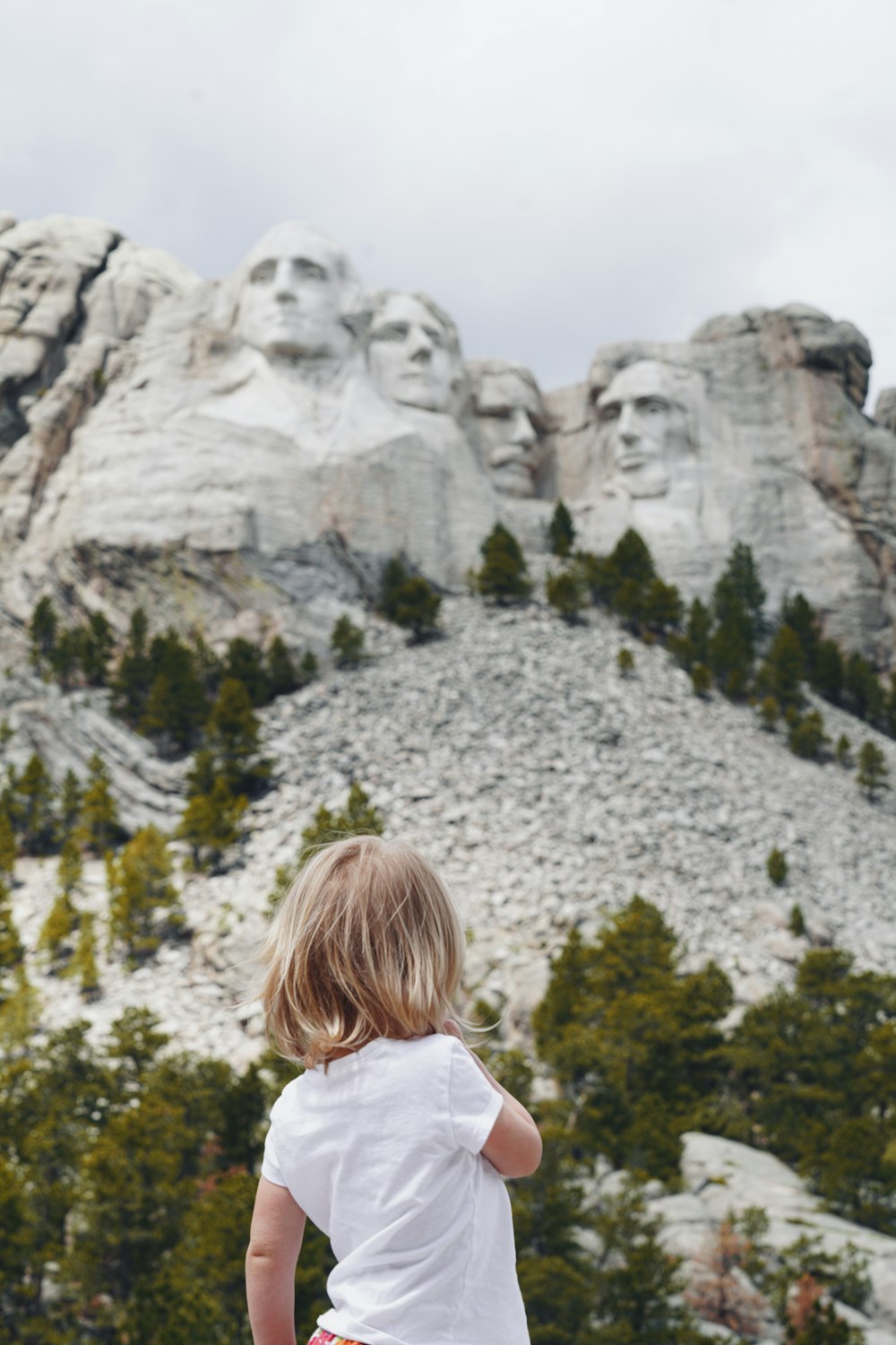 a little girl standing in front of a mountain