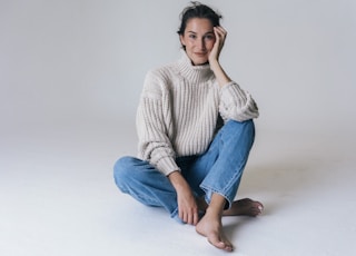 woman in gray sweater and blue denim jeans sitting on white floor