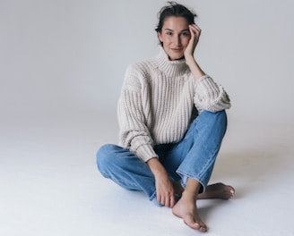 woman in gray sweater and blue denim jeans sitting on white floor