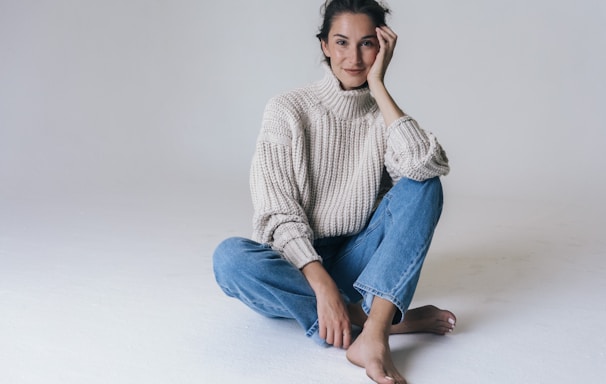woman in gray sweater and blue denim jeans sitting on white floor