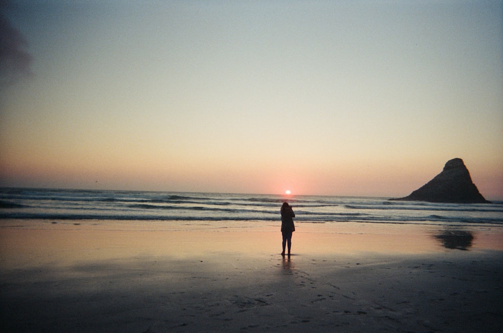 Una persona parada en una playa al atardecer