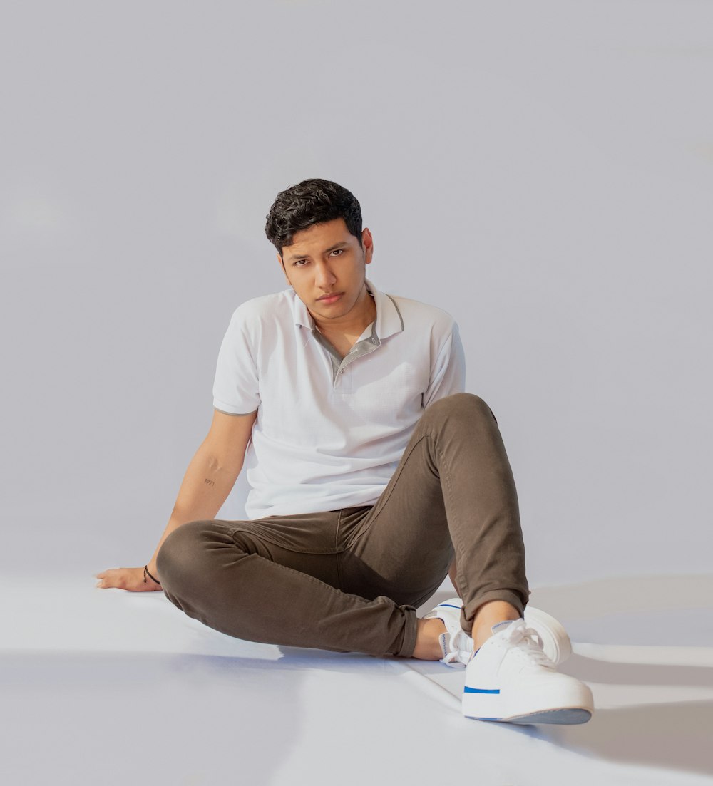 a man sitting on the ground wearing a white shirt and brown pants