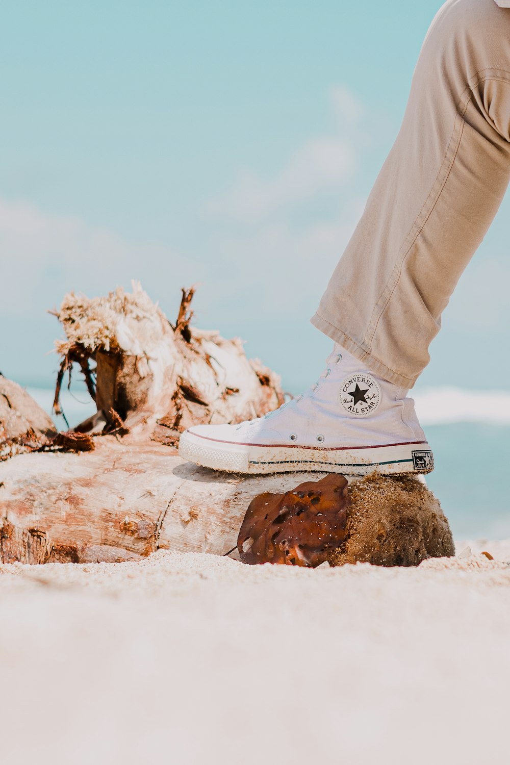 person in white pants and white sneakers standing on brown rock