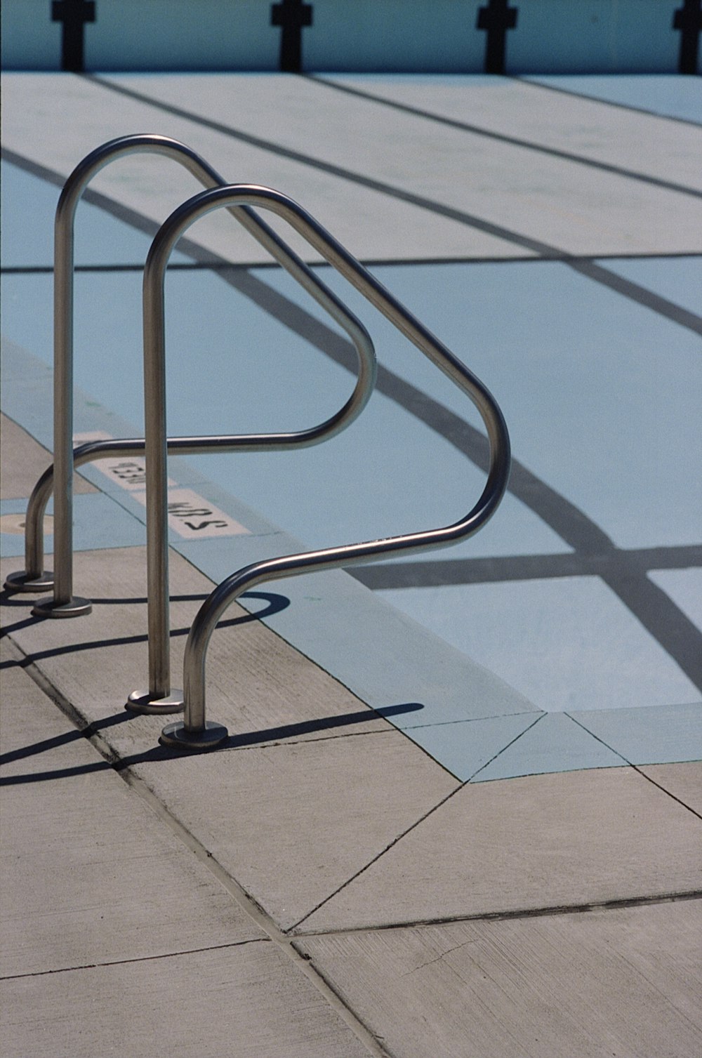 a metal railing on a sidewalk near a swimming pool