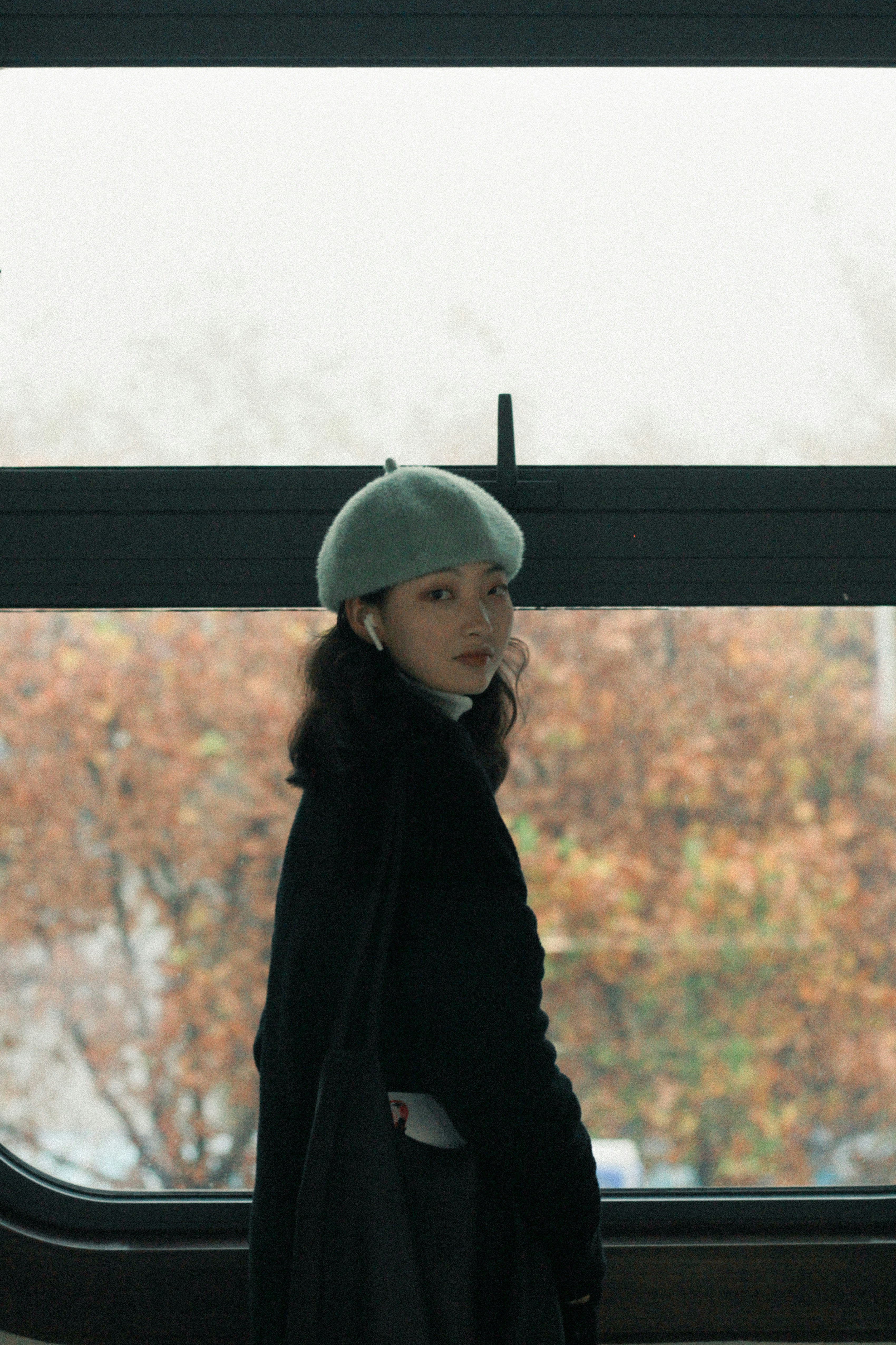a woman standing in front of a window wearing a hat