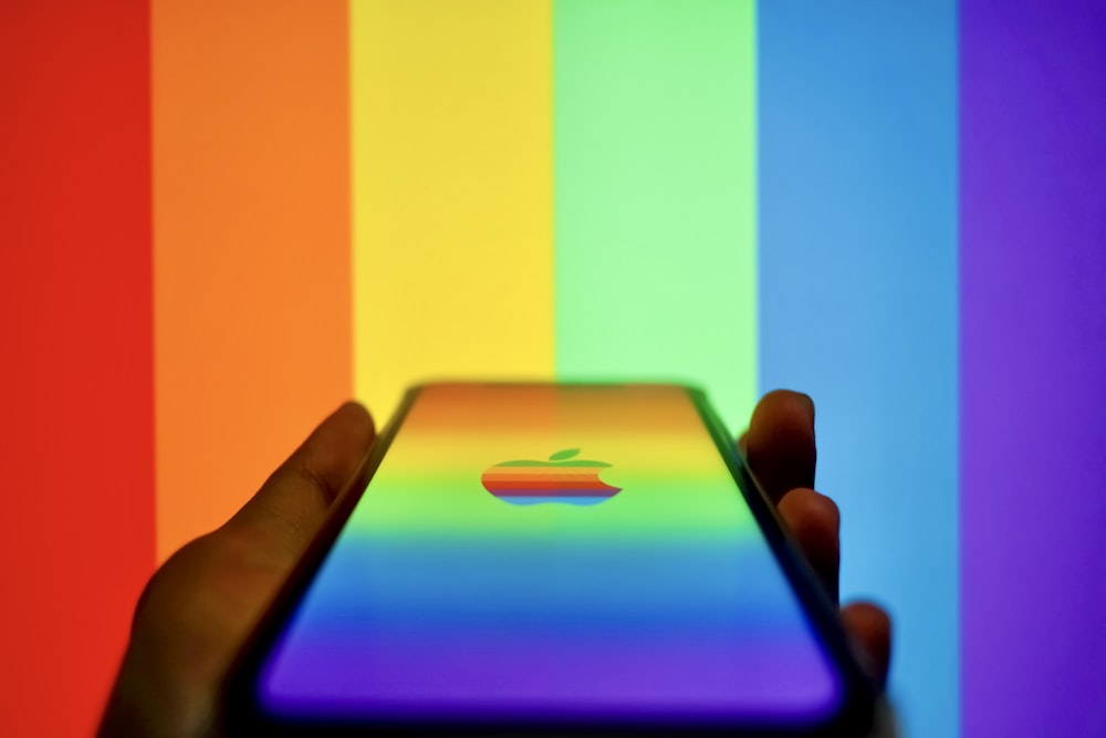Una persona sosteniendo un iPhone frente a un fondo de arco iris