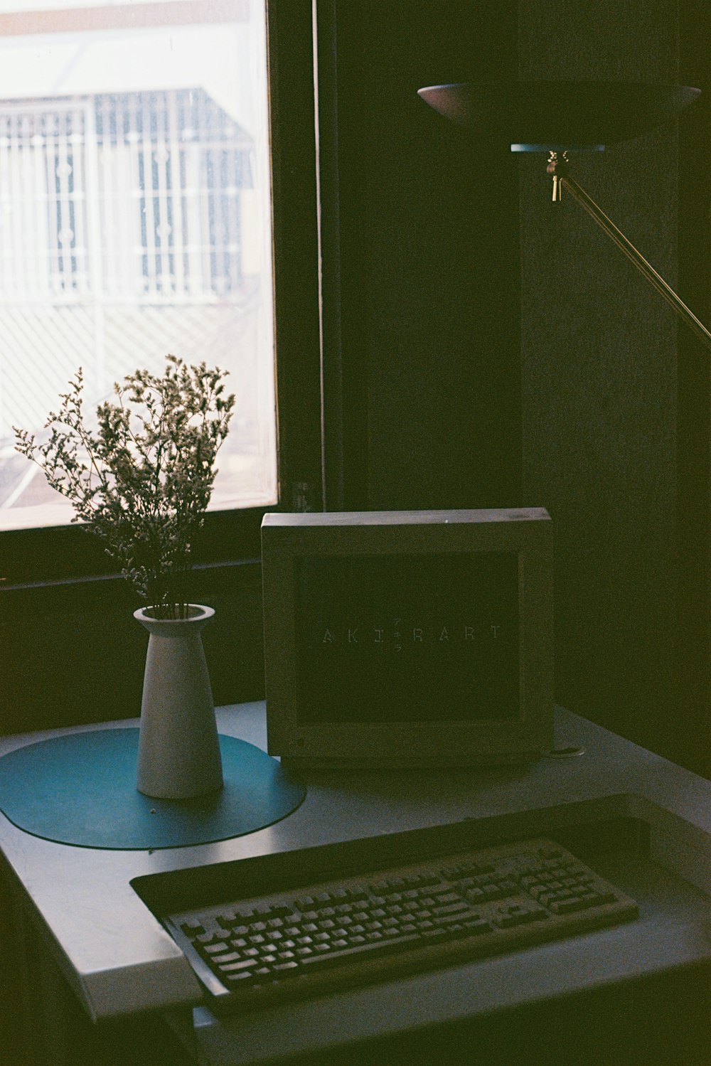 a desk with a computer and a plant in a vase