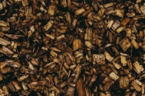 A pile of wooden chips scattered across a surface, featuring various shades of brown and textures. The pieces vary in size and shape, contributing to a rustic and organic appearance.