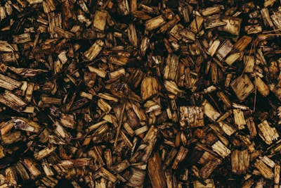A pile of wooden chips scattered across a surface, featuring various shades of brown and textures. The pieces vary in size and shape, contributing to a rustic and organic appearance.
