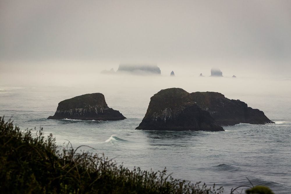 a group of rocks in the ocean on a foggy day