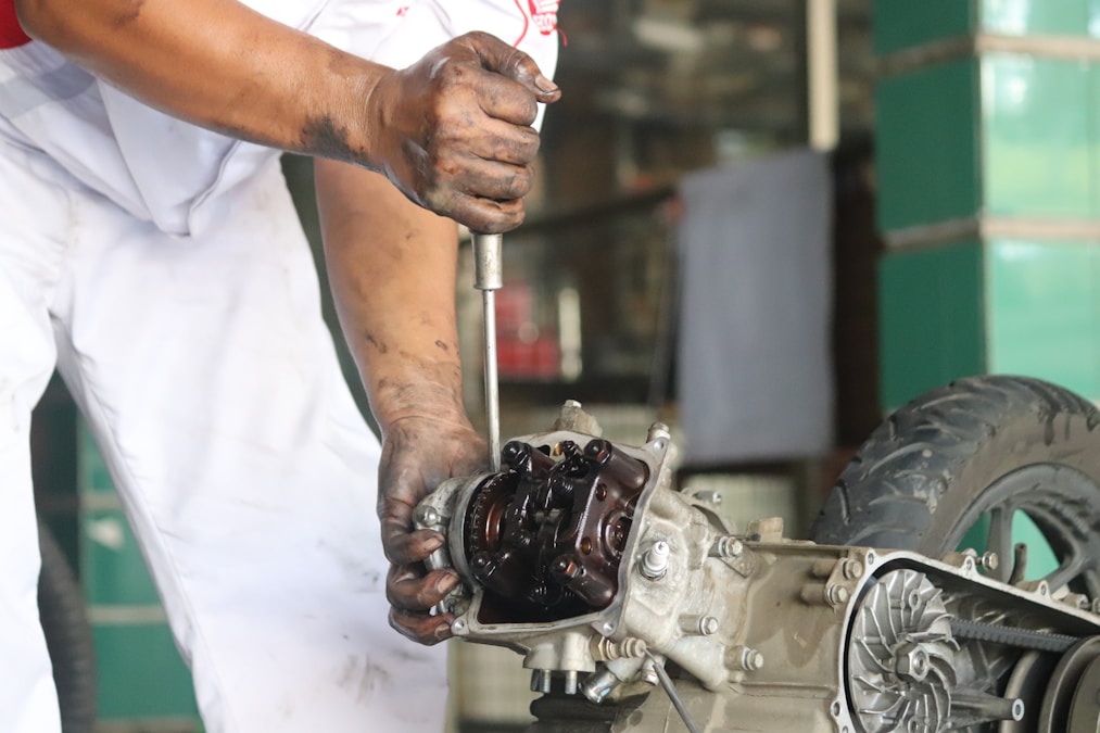 Mechanic with oily hands using a wrench on an open motorcycle engine in a workshop