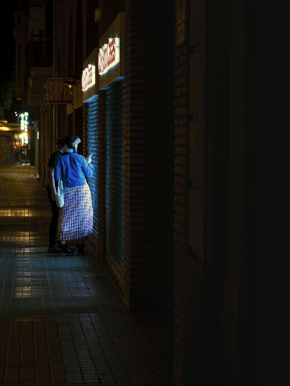 man in blue and white plaid dress shirt walking on sidewalk during night time