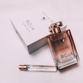 A luxurious perfume presentation including a glass bottle of perfume with a metallic cap, a white box with branding, and a smaller test vial. The setup conveys elegance and sophistication.