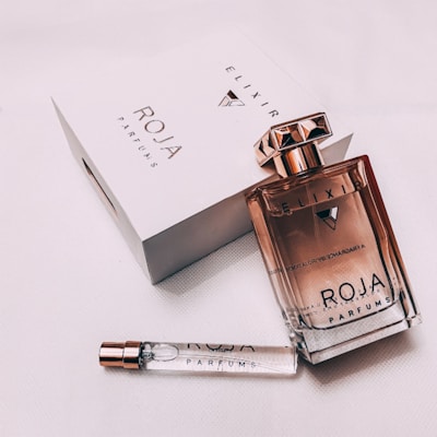 A luxurious perfume presentation including a glass bottle of perfume with a metallic cap, a white box with branding, and a smaller test vial. The setup conveys elegance and sophistication.