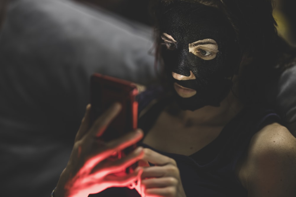 woman in black mask holding red smartphone