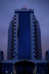 A sleek, modern skyscraper at dusk reflecting warm golden light against a deep midnight blue sky.