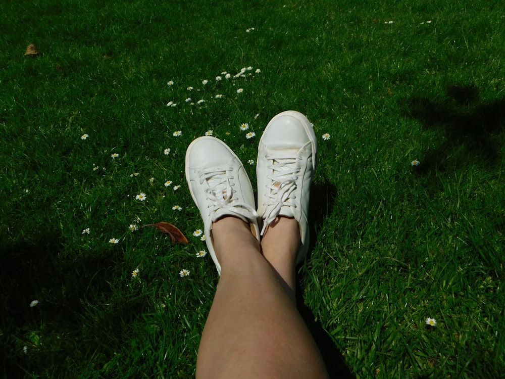 a person wearing white tennis shoes sitting in the grass