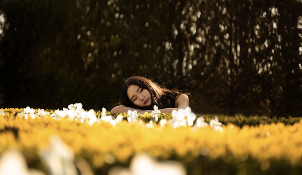 woman in white tank top lying on yellow flower field during daytime