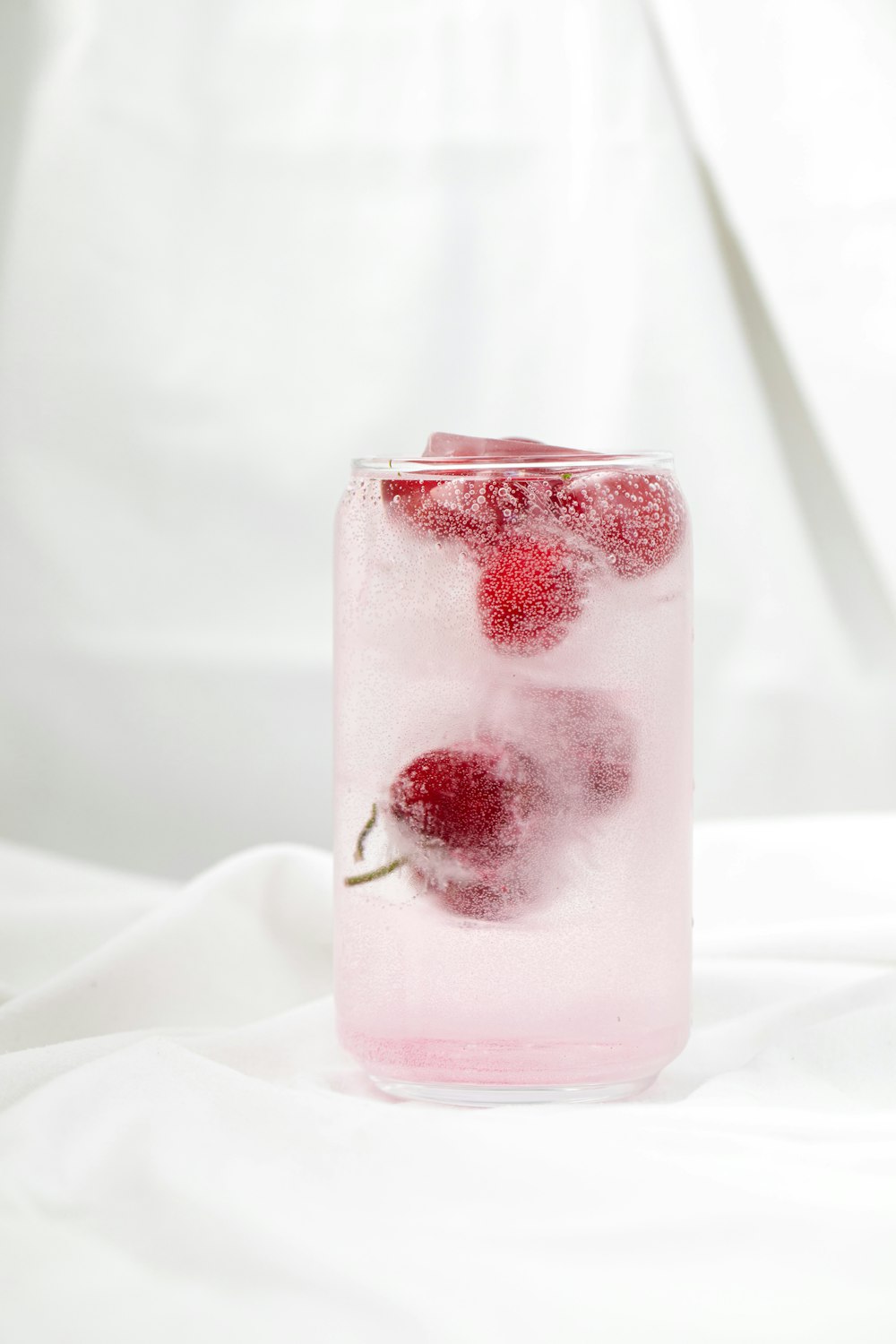 a glass filled with ice and raspberries on top of a bed