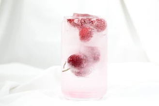 A vibrant, refreshing glass of iced fruit drink with condensation droplets, set against a clean, bright background.