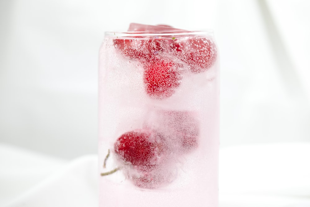 a glass filled with ice and raspberries on top of a table