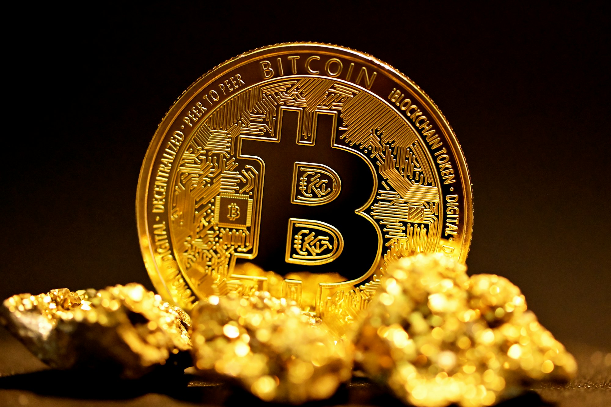 A single bitcoin surrounded by raw gold pieces.