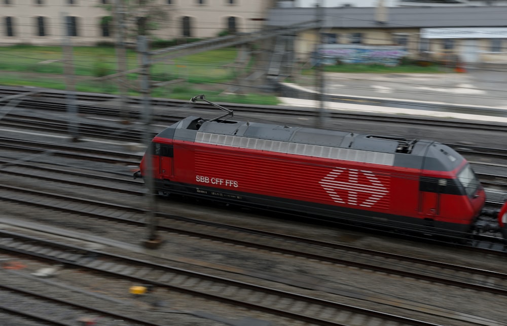 um trem vermelho viajando pelos trilhos do trem ao lado de um prédio