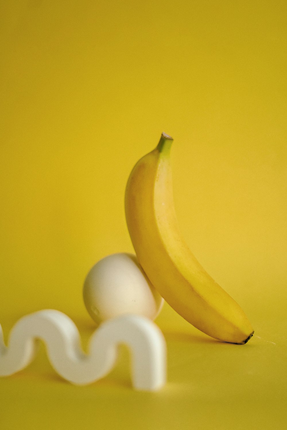 Eine Banane sitzt neben einem Ei auf gelbem Hintergrund