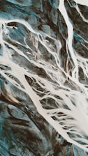 An aerial view of a river delta with white streams of water weaving through dark sandy terrain, creating a network of intricate patterns and textures.