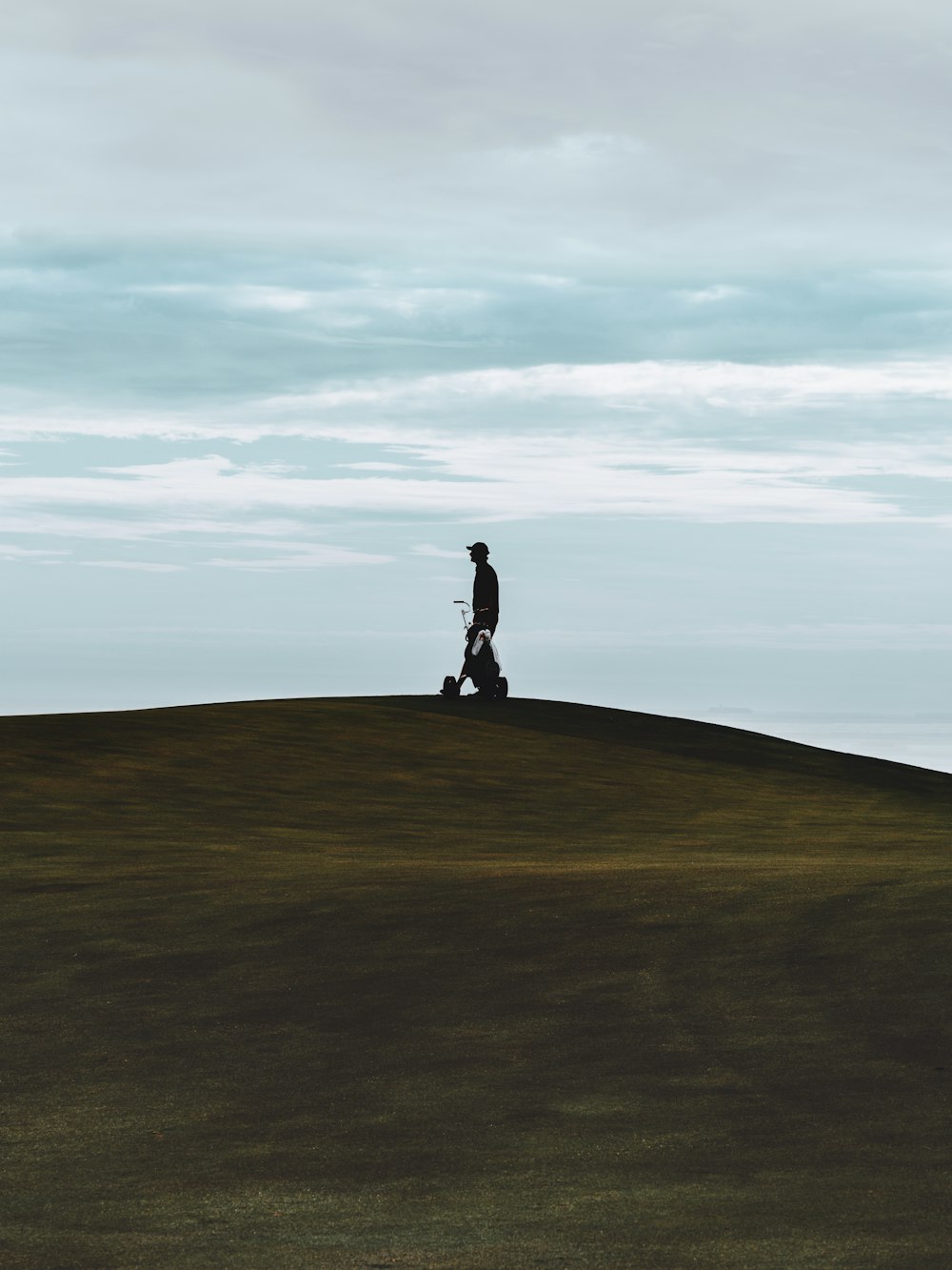 silhouette of person standing on green grass field under white clouds during daytime