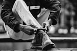 Black and white image capturing a runner tying shoelaces, ready to start the race.