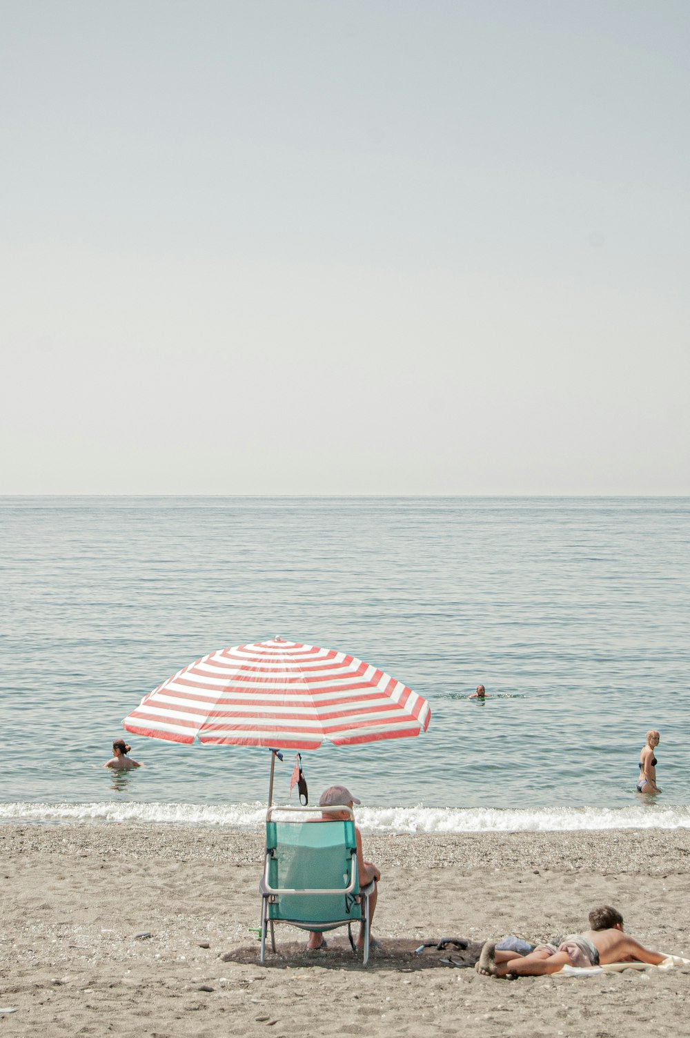 Ein paar Leute sitzen oben auf einem Strand unter einem Sonnenschirm