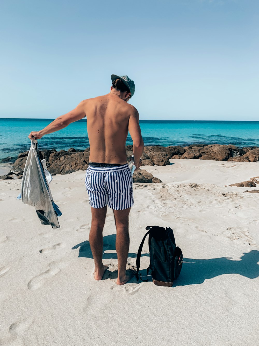 a man standing on a beach next to a bag