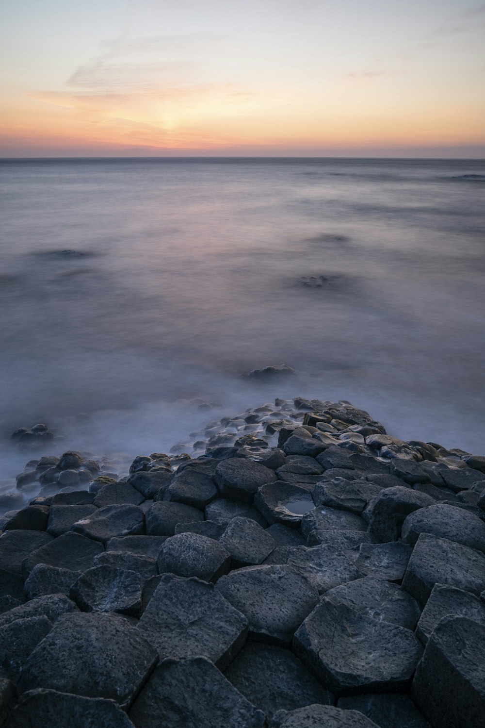 ein felsiger Strand mit Felsen im Vordergrund und einem Sonnenuntergang im Hintergrund