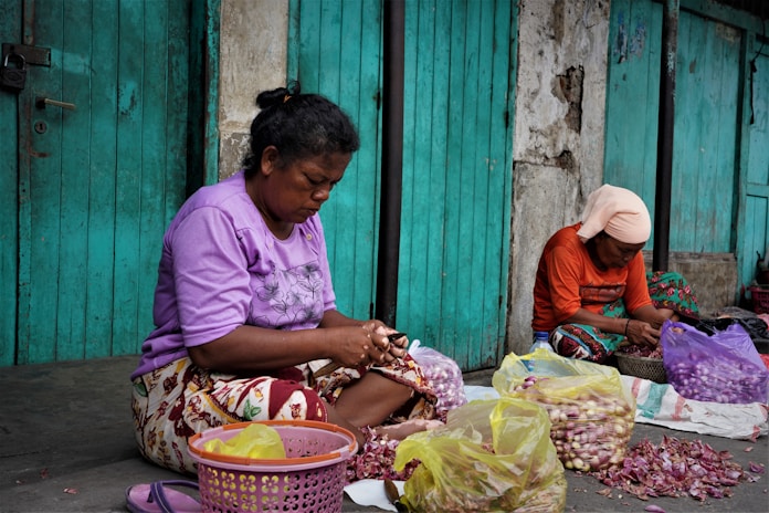 a couple of women sitting on the ground next to bags of food